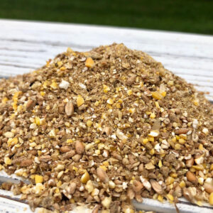 Pile of mixed birdseed with corn, seeds, and nuts on a whitewashed wooden table outdoors.