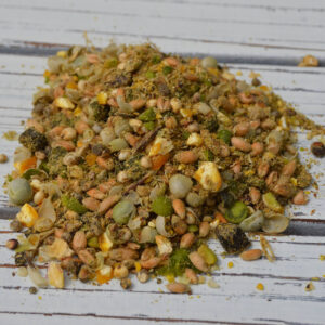 Pile of mixed birdseed on a white wooden surface, showing seeds, grains, and small dried bits scattered together, close-up.
