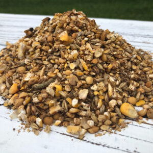 Pile of mixed birdseed (sunflower seeds, corn, millet) on a white wooden table outdoors