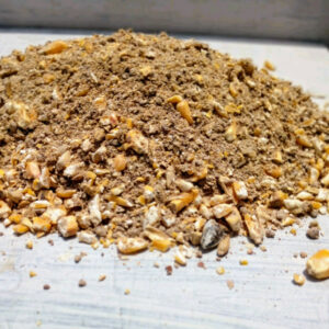 Pile of ground nuts and碎 shells mixed with brown powder on a light surface, looks like crushed nut mix or mulch.