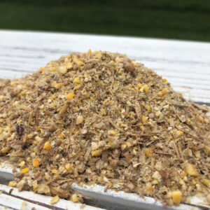 Pile of mixed crushed nuts, shells, and seeds on a weathered white wooden table outdoors.
