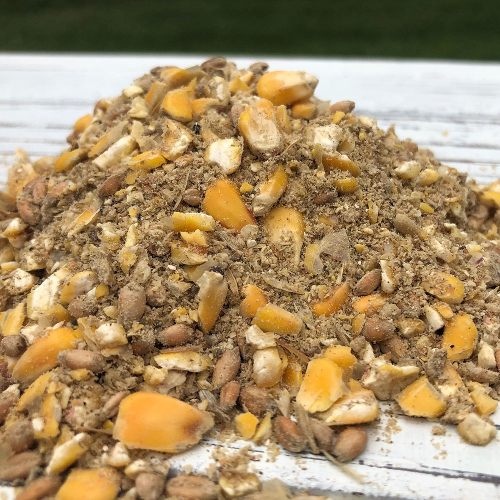 Pile of crushed mixed nuts and small dried fruit pieces on a white wooden surface.
