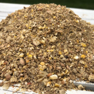 Pile of crushed nuts and seeds on a white tray, resembling trail mix in texture and color.