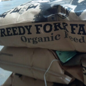 Stack of brown paper bags labeled Organic Feed with a USDA Organic sticker and bold black lettering visible on the bags