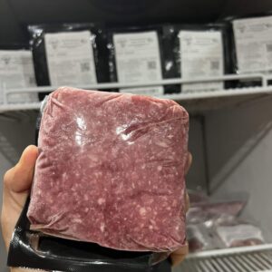 Hand holding a vacuum-sealed block of raw beef with visible marbling in a grocery store meat department